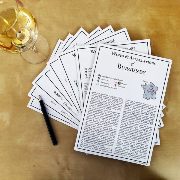 Cards detailing the wines and appellations of Burgundy, alongside a glass of white wine and a pen on a wooden table.