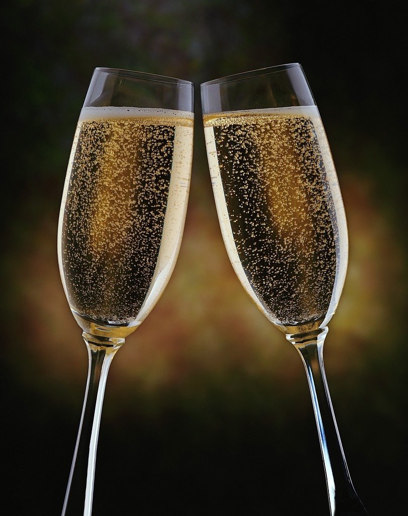 Two champagne flutes filled with sparkling wine, clinking together in a celebratory toast against a dark, blurred background.