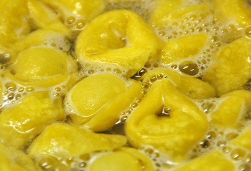 Close-up view of yellow tortellini pasta boiling in water with bubbles forming around them.