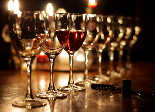 Multiple wine glasses lined up on a table, with one filled with red wine and others empty, set against a dimly lit background.