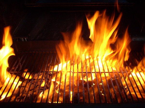 A grill with hot, roaring flames and burning charcoal beneath the grill grates, ready for cooking.