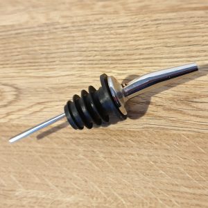 Metal liquor pourer with black rubber fins lying on a wooden surface.