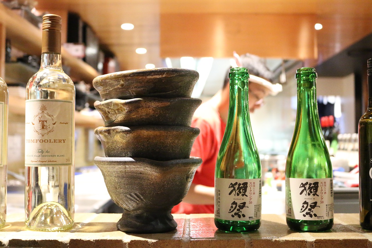 A wall with a bottle of wine, four bowls stacked and two bottles of a Japanese drink.