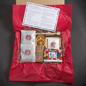 Open gift box with a DIY gin-making kit, including packets, dried orange slices, a booklet, and an instruction card.