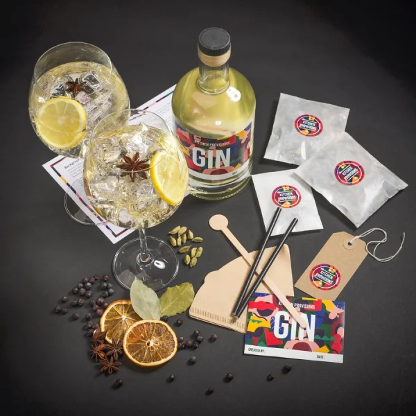 Various gin-making ingredients and tools arranged with a bottle of gin and two garnished gin cocktails.