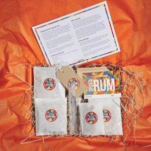 Spiced rum making kit components laid out in a box with an orange background, including ingredients, instructions, and tools.