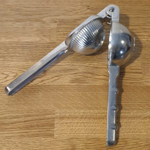 Metal citrus juicer with handles open, resting on a wooden surface.