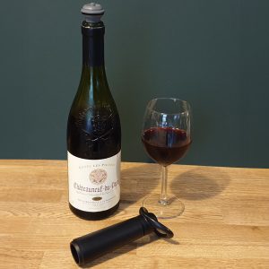 Wine bottle with a vacuum stopper, a glass of red wine, and a black wine pump.