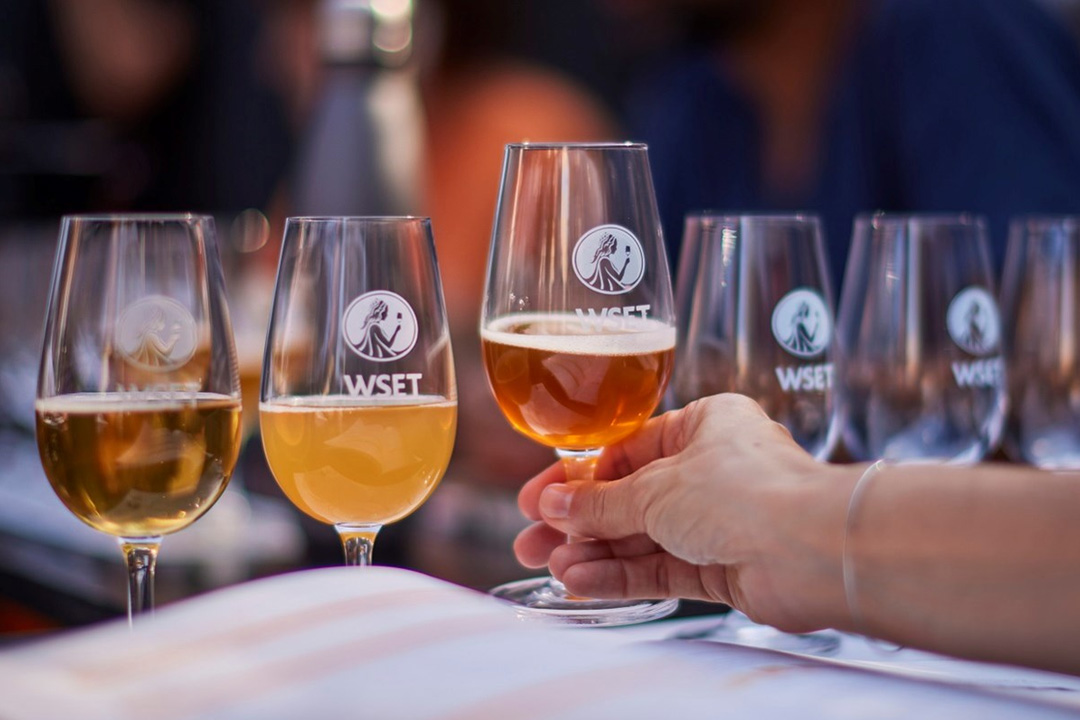 Someone picking up glass of beer, from a row of glasses with different types of beers.