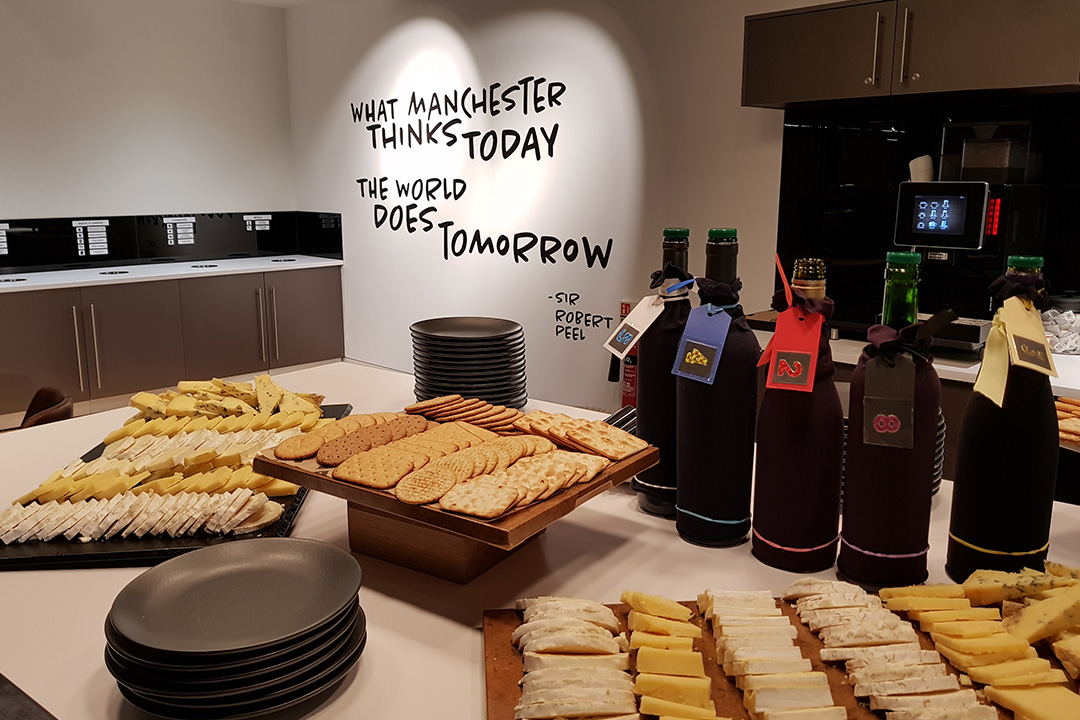 2 platters of cheese, a platter of crackers, two stacks of plates and 5 bottles with the branding hidden on a table.