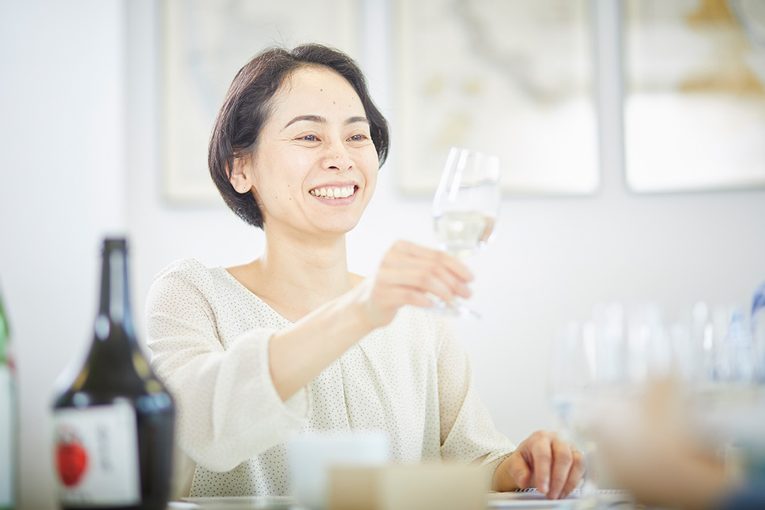 A smiling women looking at a slightly tilted glass of sake.