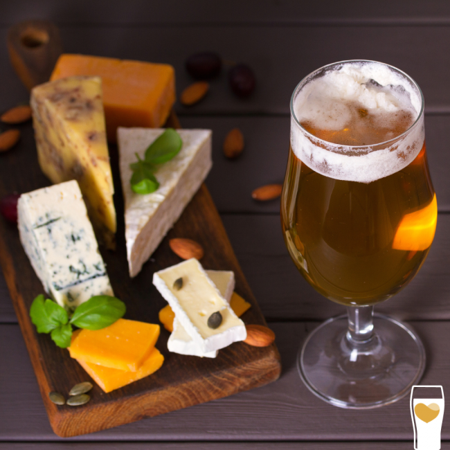 A cheeseboard featuring a selection of cheeses, nuts and fruit with a beer glass next to it.